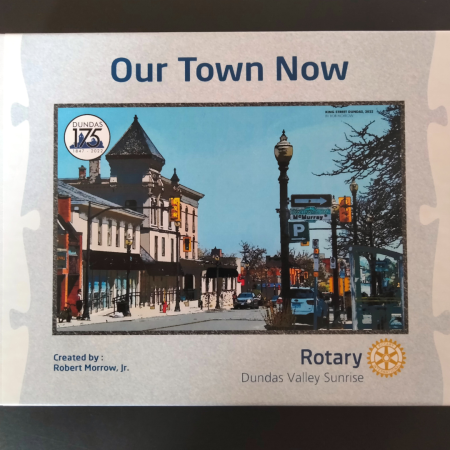 The image is of a cardboard box holding a puzzle. The front reads "Our Town Now" and there is a photograph taken recently of King St. W in Dundas, ON. In the top left corner of the image is the Dundas 175 logo.