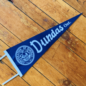 A blue pennant with white lettering and a white seal that reads "Corporation of Dundas, Inc. 1847" on a wooden floor.